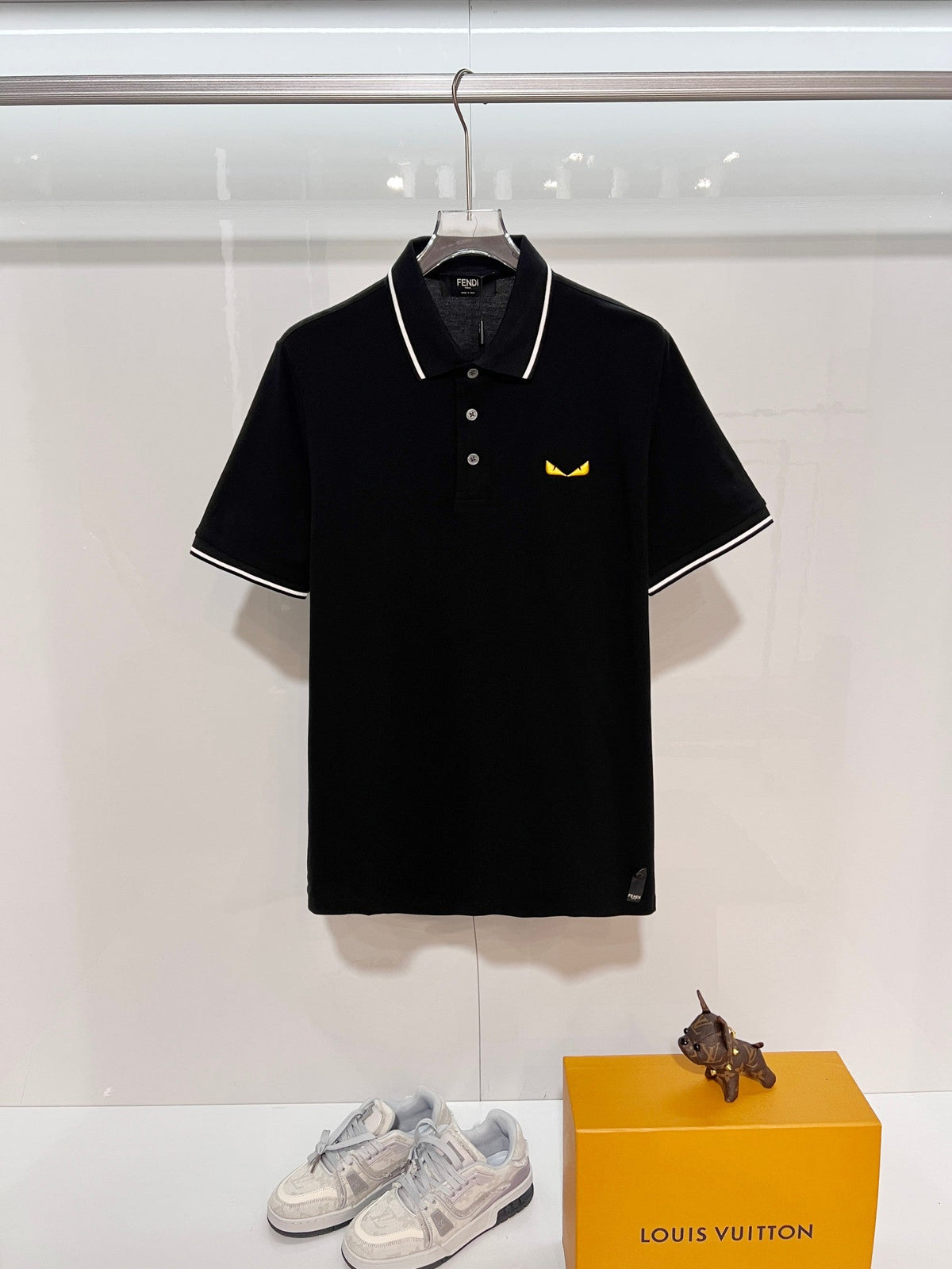 A polo shirt with embroidered letters on the eyes of a golden little monster on the chest