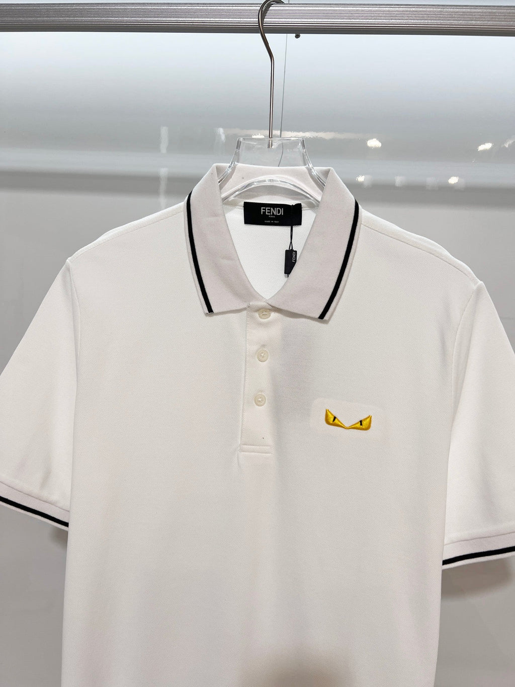 A polo shirt with embroidered letters on the eyes of a golden little monster on the chest
