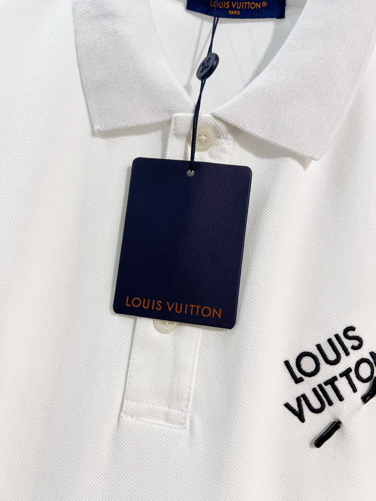 A polo shirt with embroidered letters on the eyes of a golden little monster on the chest