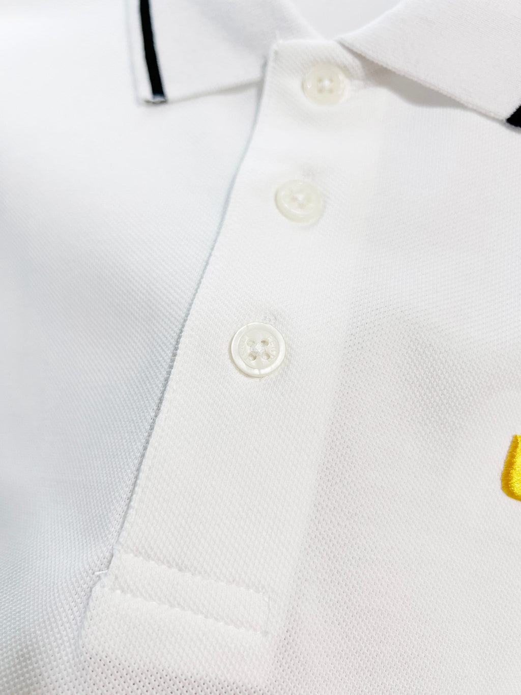 A polo shirt with embroidered letters on the eyes of a golden little monster on the chest