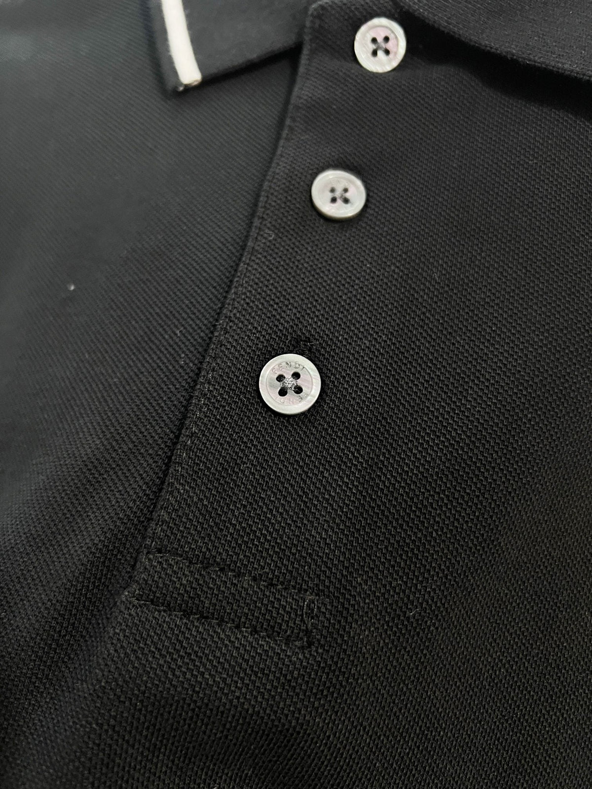 A polo shirt with embroidered letters on the eyes of a golden little monster on the chest