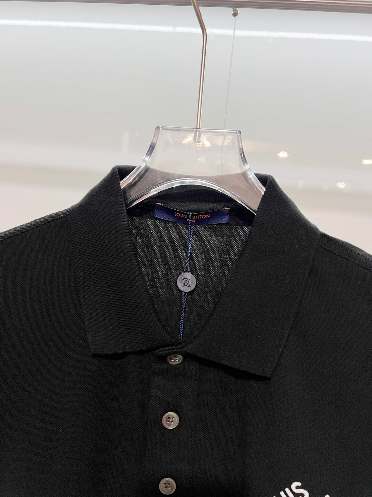 A polo shirt with embroidered letters on the eyes of a golden little monster on the chest